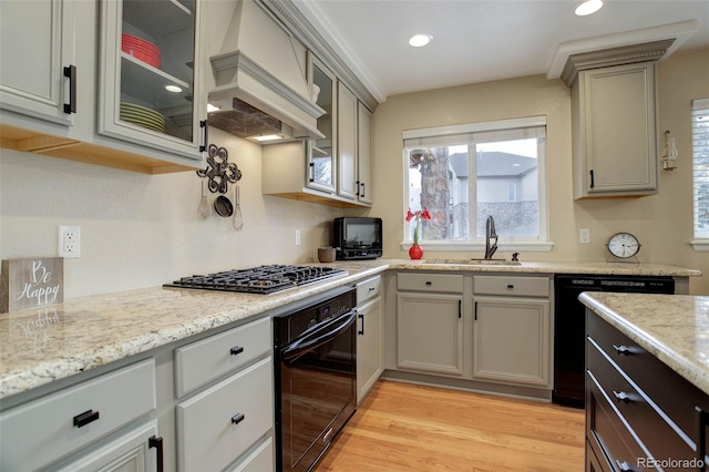 kitchen with a sink, plenty of natural light, light wood-style flooring, custom exhaust hood, and black appliances