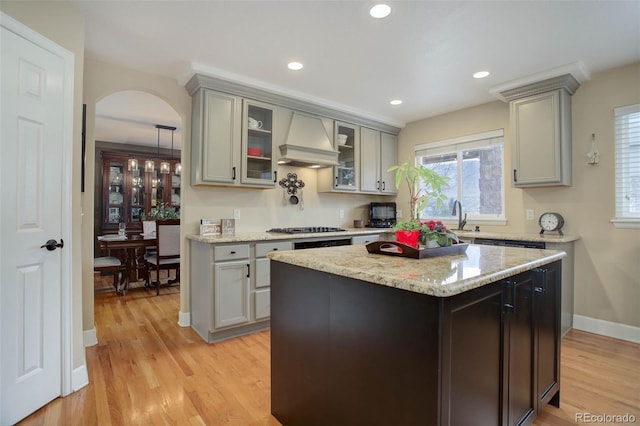 kitchen with gray cabinetry, arched walkways, stainless steel gas stovetop, and custom range hood
