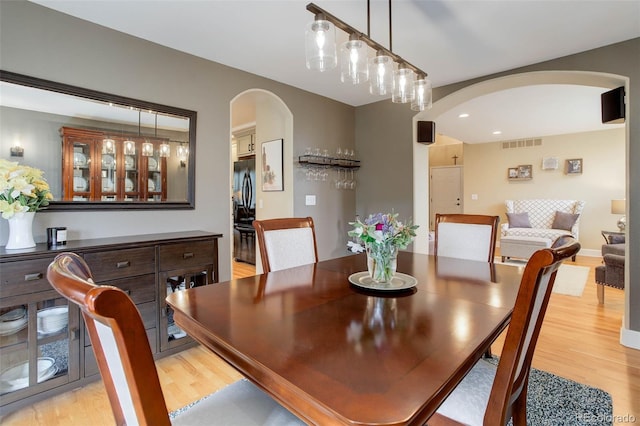 dining space with visible vents, arched walkways, and light wood finished floors