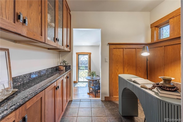 kitchen with brown cabinetry, healthy amount of natural light, glass insert cabinets, and dark stone counters
