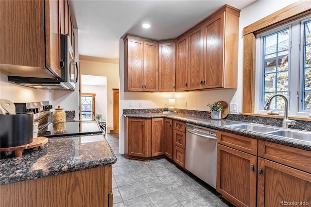 kitchen featuring appliances with stainless steel finishes, a sink, dark stone counters, brown cabinetry, and recessed lighting