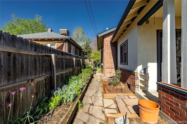 view of property exterior with brick siding, stucco siding, fence, and a garden