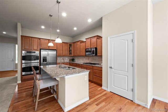 15414 Xenia Ct, Thornton, CO 80602 - kitchen featuring stainless steel appliances, brown cabinets, an island with sink, light stone counters, and light wood-type flooring