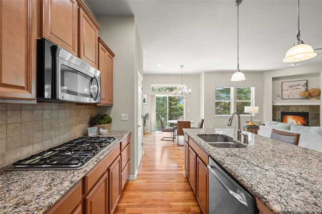 15414 Xenia Ct, Thornton, CO 80602 - kitchen featuring stainless steel appliances, light wood finished floors, brown cabinetry, a tile fireplace, and light stone countertops