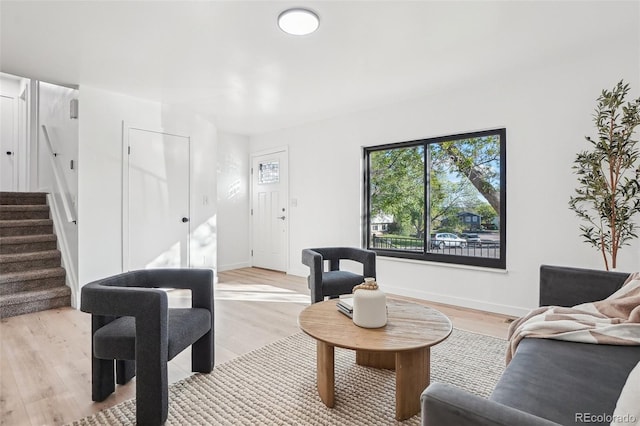 living room featuring stairs, light wood-style flooring, and baseboards