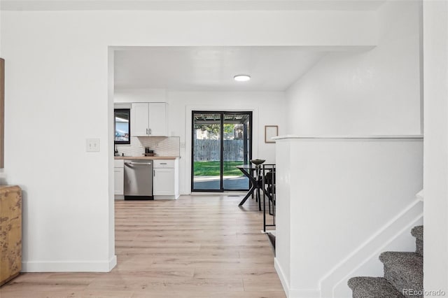 hall featuring light wood-style floors, baseboards, and stairs
