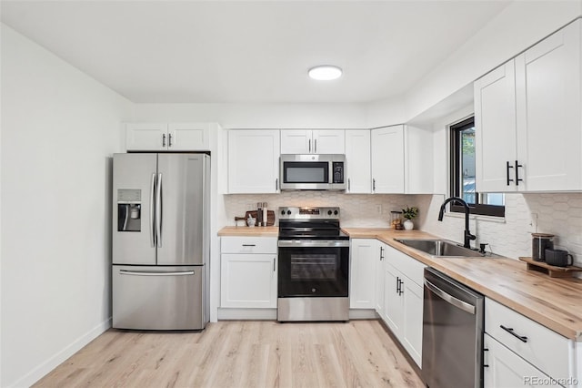 kitchen with stainless steel appliances, butcher block countertops, a sink, light wood-style floors, and white cabinetry