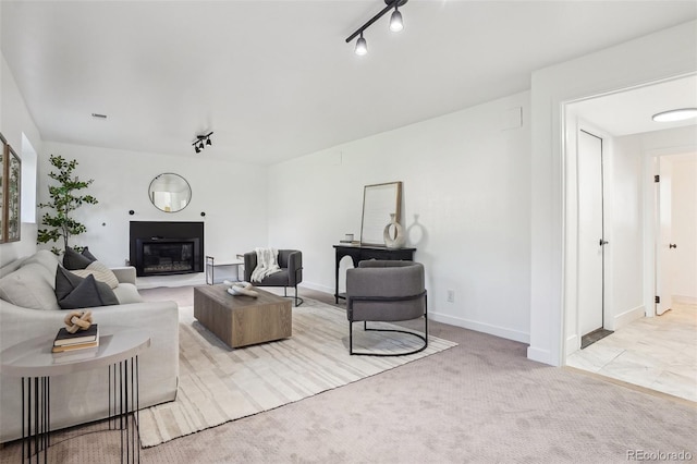 living area with track lighting, a glass covered fireplace, light carpet, and baseboards