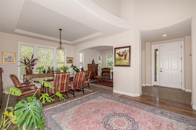 entrance foyer featuring arched walkways, baseboards, wood finished floors, and a tray ceiling