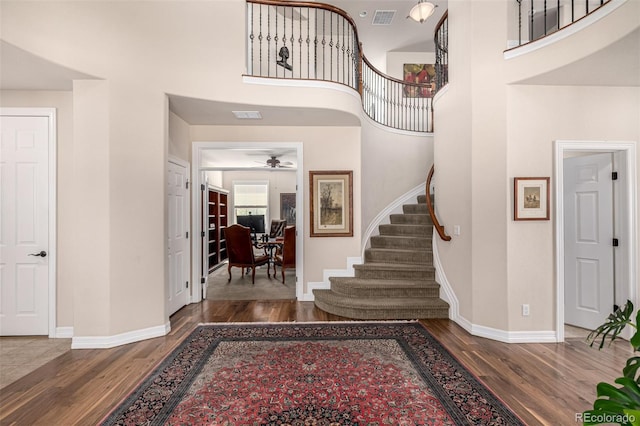 entryway featuring wood finished floors, stairway, baseboards, a ceiling fan, and a towering ceiling