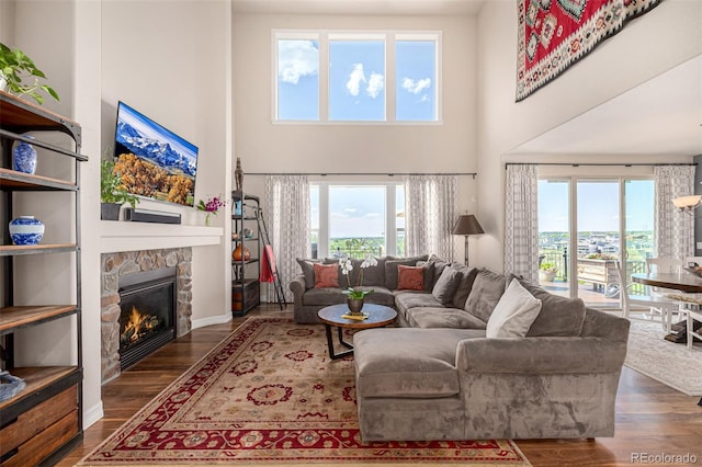 living room featuring a high ceiling, wood finished floors, a stone fireplace, and baseboards