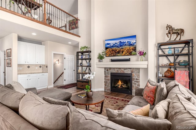 living room featuring wood finished floors, baseboards, a towering ceiling, a fireplace, and recessed lighting