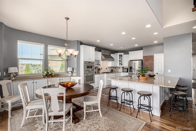 kitchen with stainless steel appliances, wall chimney range hood, white cabinetry, a center island with sink, and recessed lighting