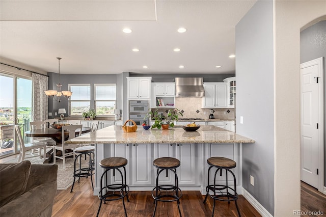 kitchen featuring wall chimney range hood, white cabinetry, dark wood-style floors, a breakfast bar, and recessed lighting