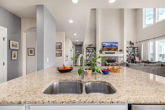 kitchen featuring a sink, open floor plan, light stone countertops, a fireplace, and recessed lighting