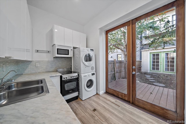 kitchen featuring a healthy amount of sunlight, sink, electric range, stacked washer / dryer, and white cabinets