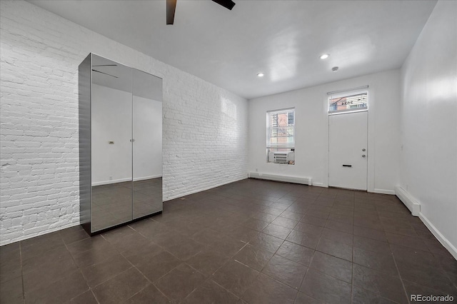 empty room featuring a baseboard radiator, ceiling fan, cooling unit, and brick wall