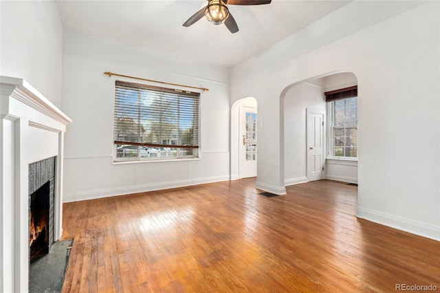 1748 S Logan St, Denver, CO 80210 - unfurnished living room with a warm lit fireplace, a ceiling fan, hardwood / wood-style floors, arched walkways, and baseboards