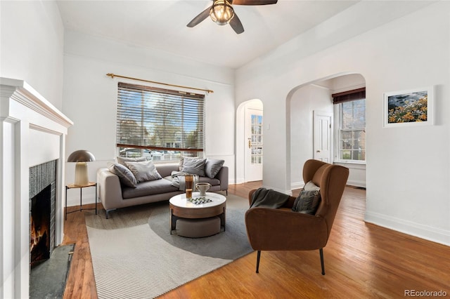 1748 S Logan St, Denver, CO 80210 - living room featuring arched walkways, a warm lit fireplace, a ceiling fan, baseboards, and wood finished floors