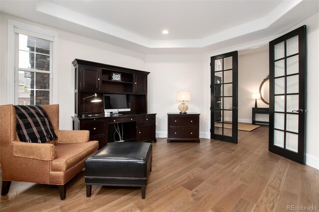 living area with a tray ceiling, light hardwood / wood-style floors, and french doors