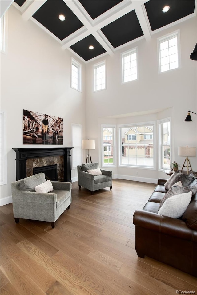 living room with coffered ceiling, a towering ceiling, a premium fireplace, and light hardwood / wood-style floors