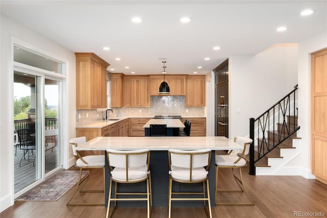 kitchen with a center island, a kitchen breakfast bar, dark hardwood / wood-style floors, pendant lighting, and backsplash