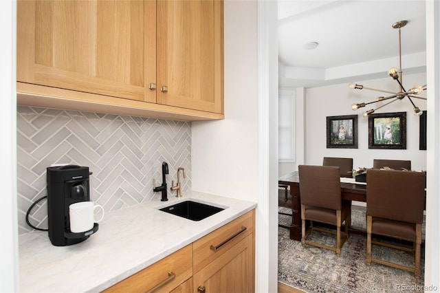 kitchen with sink, a chandelier, hanging light fixtures, light stone countertops, and decorative backsplash