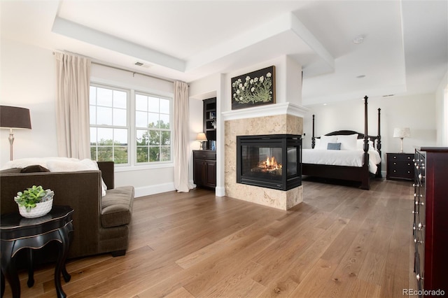 bedroom with a multi sided fireplace, wood-type flooring, and a tray ceiling