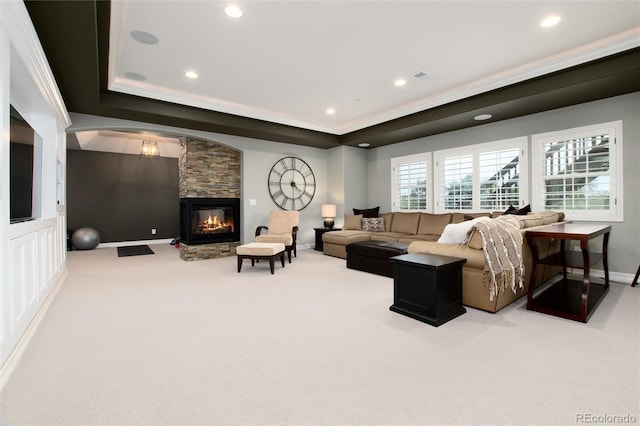 carpeted living room with a stone fireplace and a raised ceiling