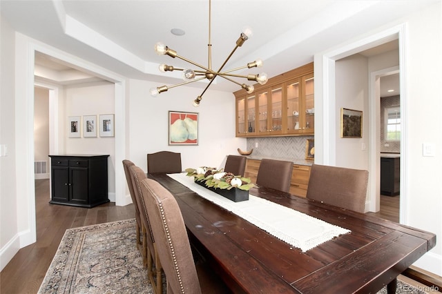 dining area with an inviting chandelier, dark hardwood / wood-style flooring, and a raised ceiling