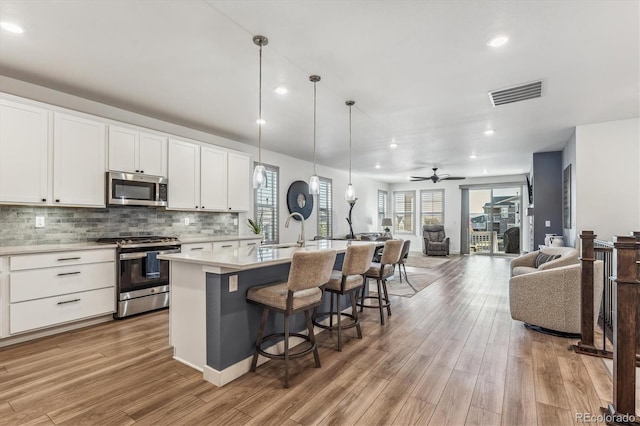 kitchen with ceiling fan, an island with sink, white cabinetry, light hardwood / wood-style floors, and stainless steel appliances