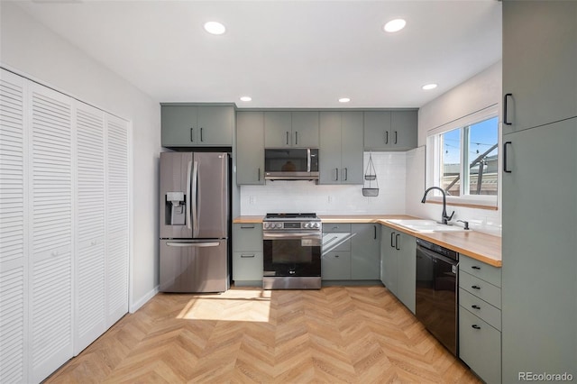 kitchen with appliances with stainless steel finishes, a sink, gray cabinetry, butcher block counters, and tasteful backsplash