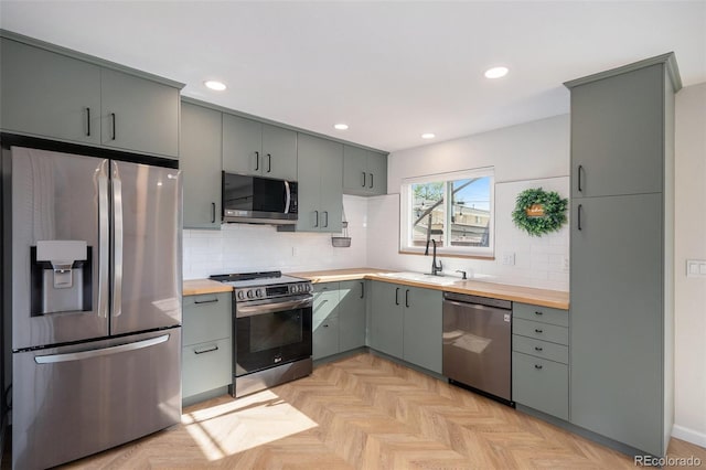 kitchen with stainless steel appliances, a sink, wood counters, gray cabinets, and backsplash