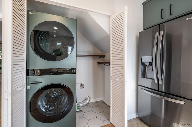 laundry room featuring stacked washer / dryer, baseboards, and light tile patterned floors