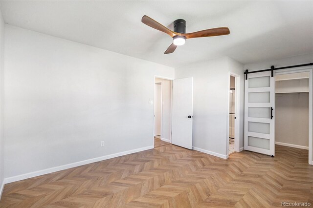 unfurnished bedroom featuring a spacious closet, ensuite bathroom, a barn door, baseboards, and a closet