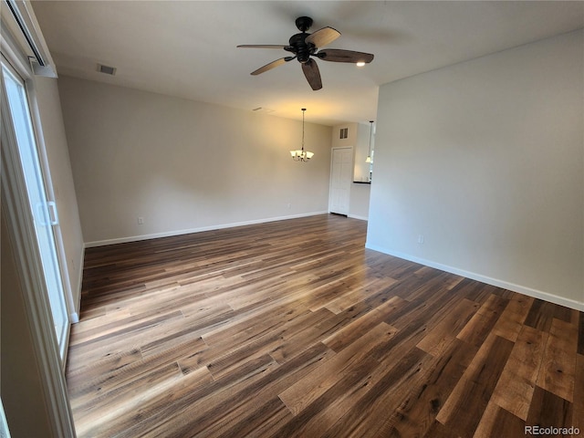 spare room with baseboards, dark wood-style flooring, visible vents, and ceiling fan with notable chandelier