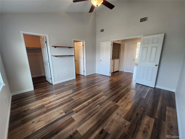 unfurnished bedroom featuring baseboards, dark wood-style flooring, visible vents, high vaulted ceiling, and a walk in closet