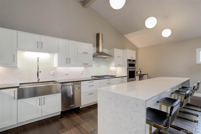 kitchen featuring lofted ceiling with beams, a kitchen bar, wall chimney exhaust hood, a sink, and stainless steel appliances