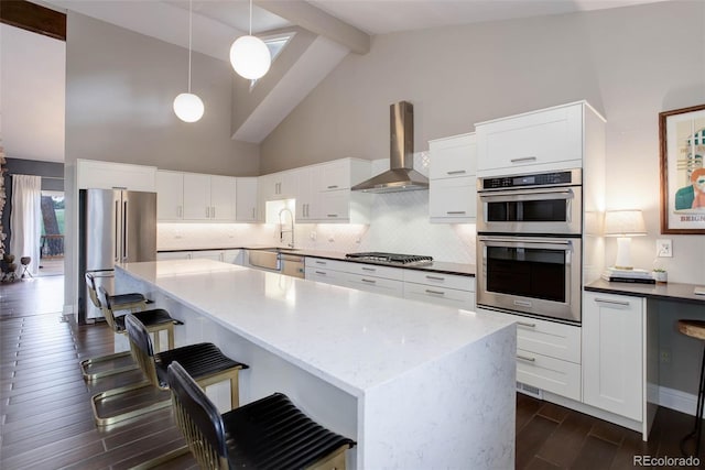 kitchen with wall chimney range hood, stainless steel appliances, decorative backsplash, beamed ceiling, and dark wood-style floors