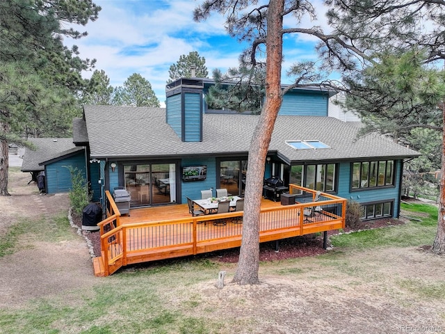back of property with a lawn, a wooden deck, roof with shingles, and a chimney