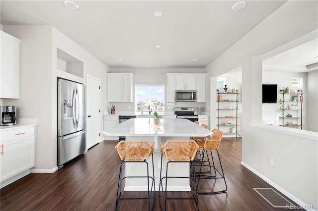 21925 E 44th Pl, Aurora, CO 80019 - kitchen featuring appliances with stainless steel finishes, a kitchen bar, light countertops, white cabinetry, and dark wood-style flooring