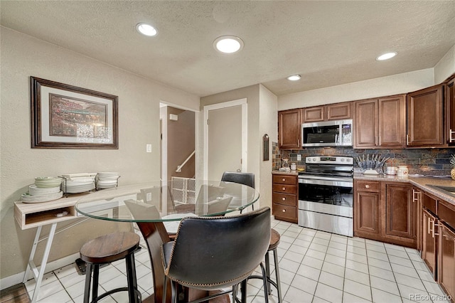 kitchen featuring tasteful backsplash, a kitchen breakfast bar, light tile patterned floors, stainless steel appliances, and a textured ceiling