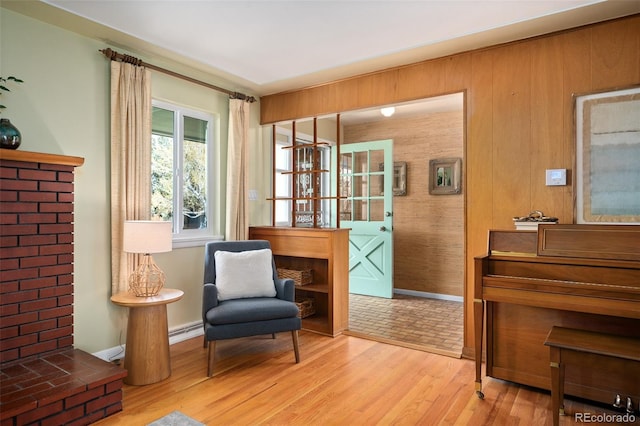 sitting room featuring a baseboard radiator, wooden walls, wood finished floors, and baseboards