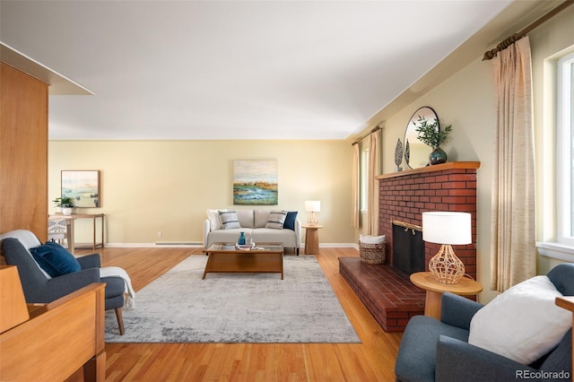 living area featuring baseboards, light wood-style flooring, a brick fireplace, and baseboard heating