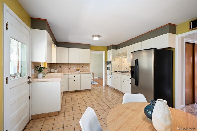 kitchen featuring black stovetop, oven, tile countertops, decorative backsplash, and stainless steel fridge