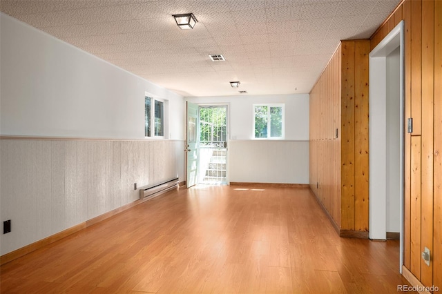 empty room with visible vents, baseboard heating, wood finished floors, and wood walls