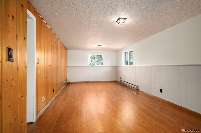 empty room featuring wood walls, baseboard heating, and wood finished floors