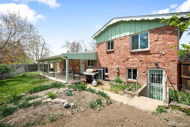 back of house with a fenced backyard, a yard, board and batten siding, a patio, and brick siding