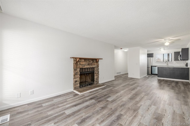 unfurnished living room with a fireplace, sink, ceiling fan, a textured ceiling, and light wood-type flooring