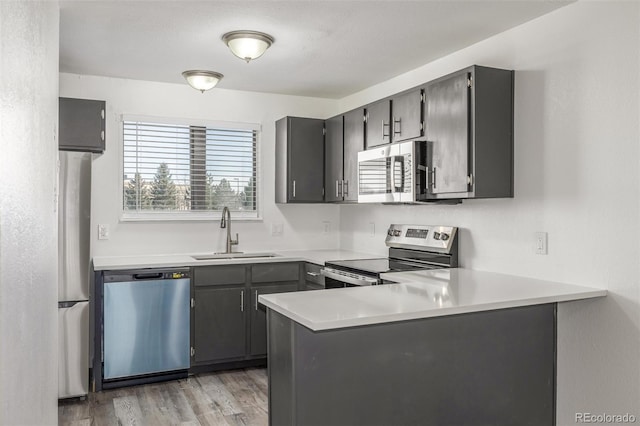 kitchen featuring sink, light wood-type flooring, appliances with stainless steel finishes, gray cabinets, and kitchen peninsula